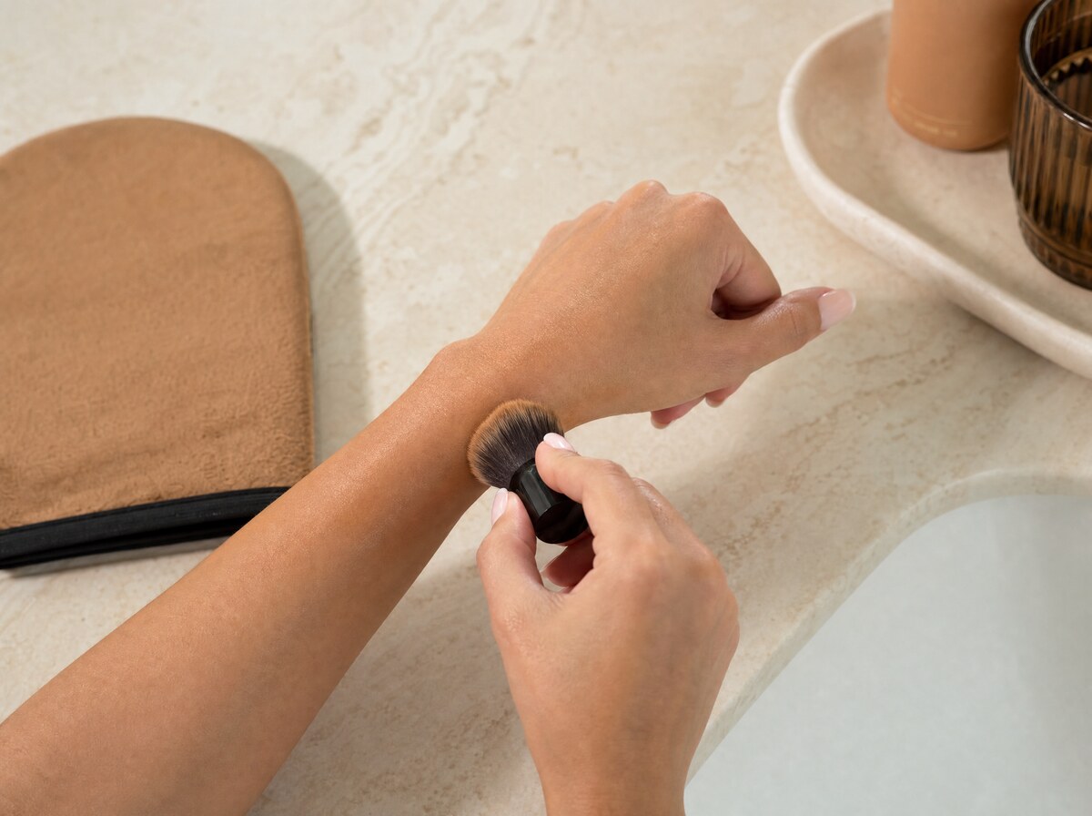 Brush blending self-tanner around wrist and hand.
